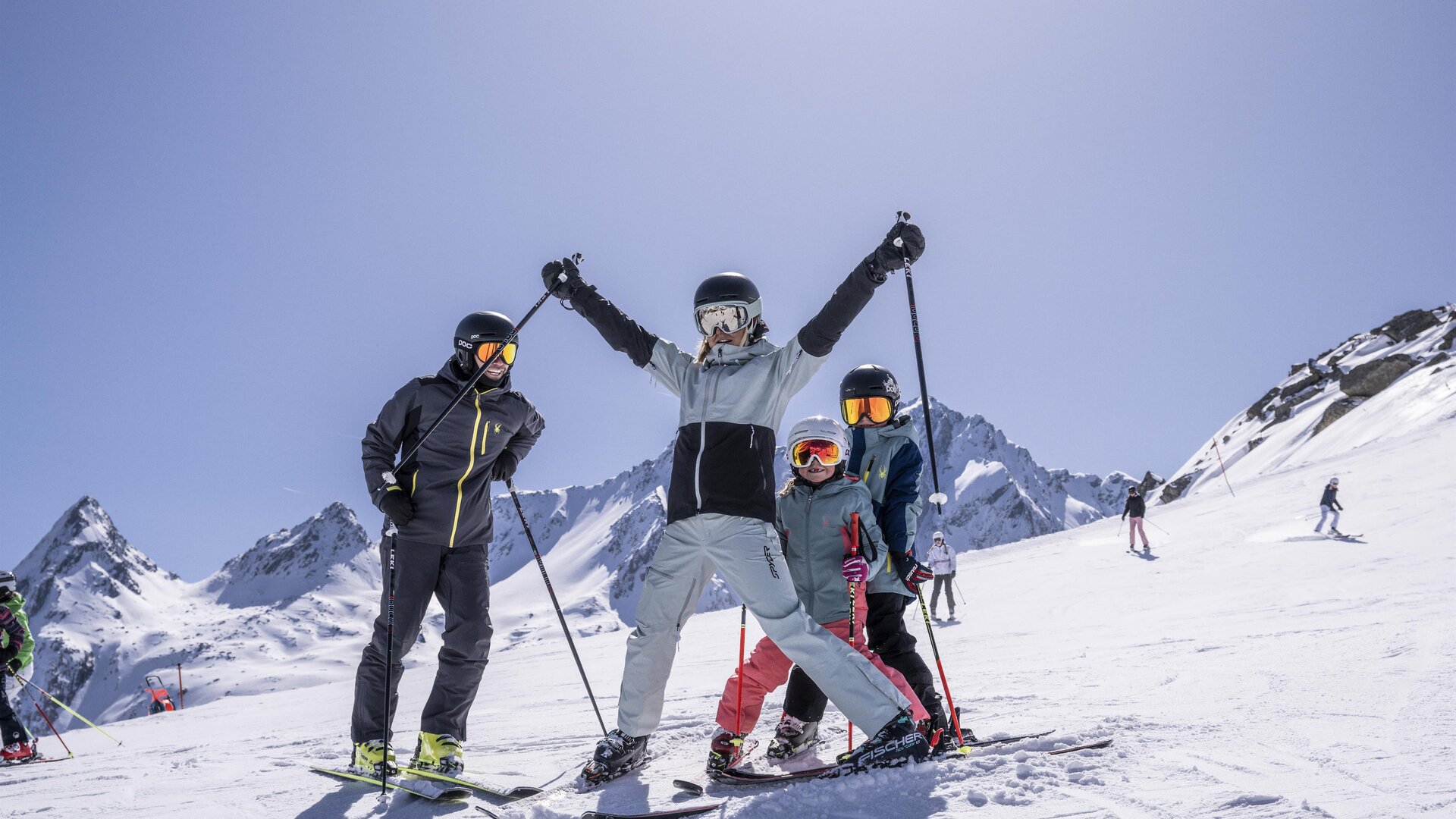 Eine Gruppe von Skifahrern steht auf einer schneebedeckten Piste in den Bergen. Die Sonne scheint und der Himmel ist klar.