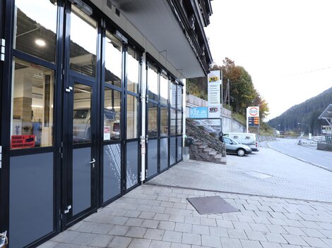 Ein modernes Geschäftshaus mit großen Fenstern und glatten Steinplatten. Im Hintergrund sind Berge und eine ruhige Straße zu sehen.
