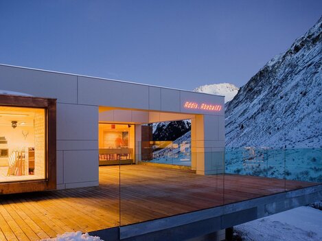A modern house in the mountains, surrounded by snow. The balcony offers a magnificent view of the surrounding mountains.