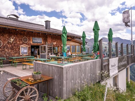 A mountain cabin with a cozy outdoor area. There are green sunshades and a beautiful view of the mountains.