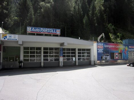 A workshop called Auto Partoll with large garage doors. In the background, there are trees and a colorful advertising board.