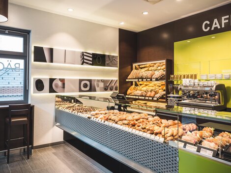 Ein modernes Café mit einer großen Auswahl an frischen Backwaren. Die hellen Farben und die einladende Atmosphäre schaffen eine gemütliche Umgebung.