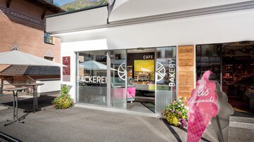 A modern bakery with large windows and an inviting entrance. In front of the shop stands a striking ice cream sign.