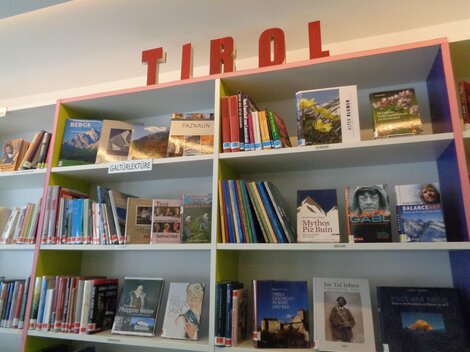 Ein Bücherregal mit vielen verschiedenen Titeln, das das Wort „TIROL“ oberhalb zeigt. Die Bücher umfassen verschiedene Themen und Genres.