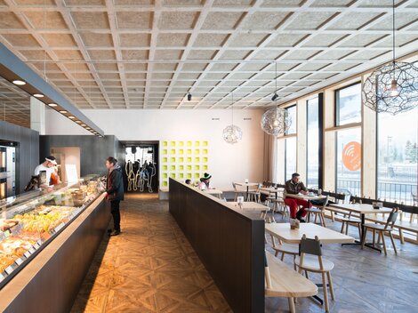 Ein modernes Café mit großen Fenstern, viel Tageslicht und einem eleganten Interieur. Die Theke ist mit verschiedenen Speisen und Getränken dekoriert. | © MPREIS Warenvertriebs GmbH