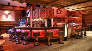 A cozy bar with wooden paneling and round stools. The lighting creates an inviting atmosphere.