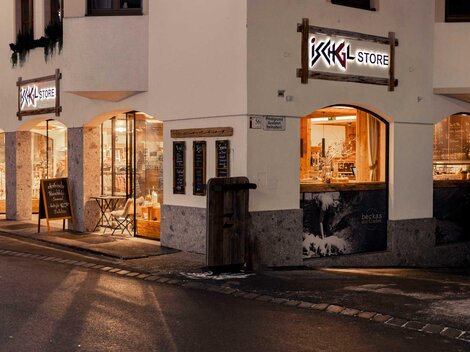 Ein Geschäft mit dem Namen "ISCHGL STORE" in einer ruhigen Straße. Die Fenster sind beleuchtet und zeigen verschiedene Produkte.