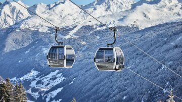Two gondolas on a cable car over snow-covered mountains. The scenery is wintry and majestic.