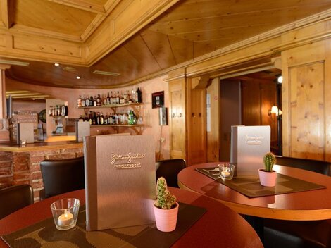 Ein gemütliches Restaurant mit Holzwänden und einer einladenden Bar. Auf den Tischen stehen Menükarten und kleine Pflanzen in Töpfen.