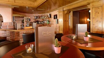 Ein gemütliches Restaurant mit Holzwänden und einer einladenden Bar. Auf den Tischen stehen Menükarten und kleine Pflanzen in Töpfen.