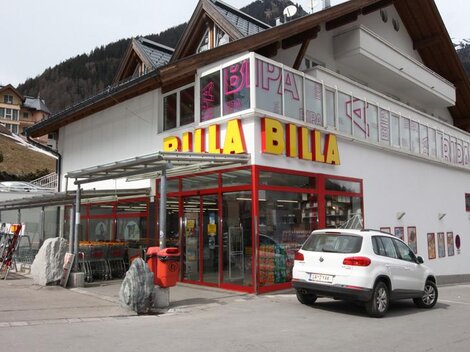 Ein Billa-Supermarkt mit einer modernen Fassade und großen Fenstern. Vor dem Geschäft steht ein weißes Auto auf einem Parkplatz.
