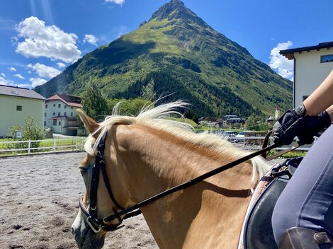 Ein Reiter sitzt auf einem Pferd mit einem schönen Berg im Hintergrund. Der Himmel ist klar und sonnig.
