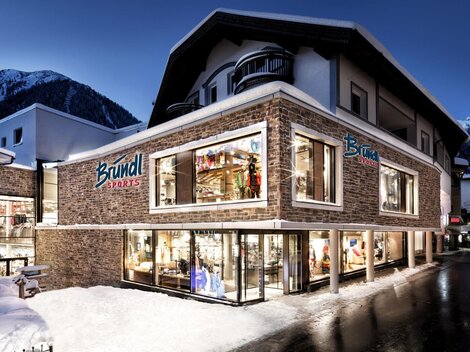Ein modernes Geschäftshaus mit großen Fenstern in den Alpen. Es ist mit Schnee umgeben und die Beleuchtung sorgt für eine gemütliche Atmosphäre bei Nacht.