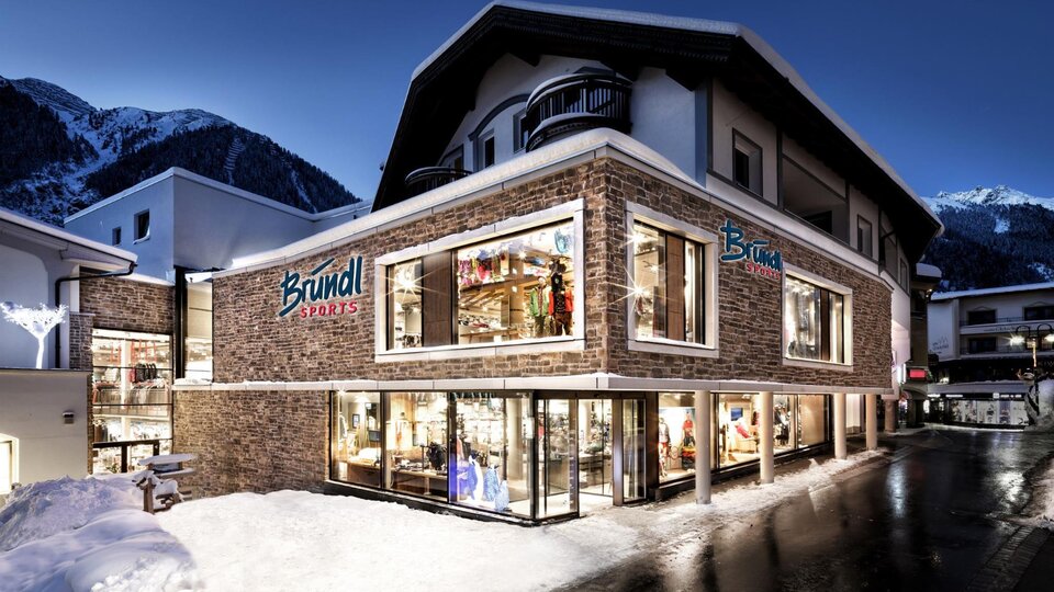 A modern commercial building with large windows in the Alps. It is surrounded by snow, and the lighting creates a cozy atmosphere at night.