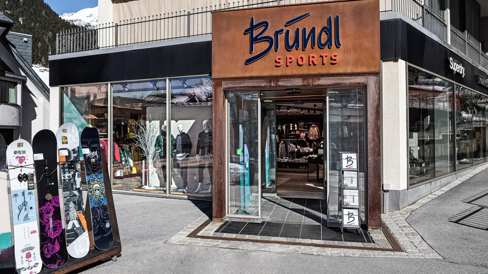 A sports store named Bründl with display windows is visible. Outside, there are some snowboards.