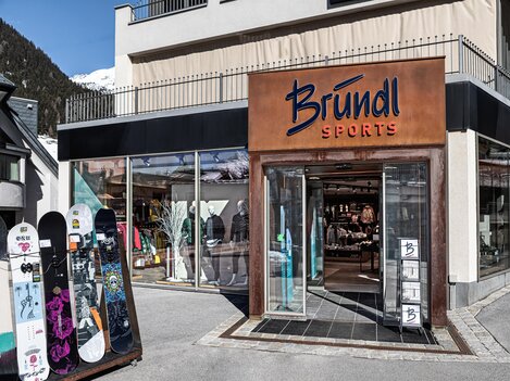 A sports store named Bründl with display windows is visible. Outside, there are some snowboards.