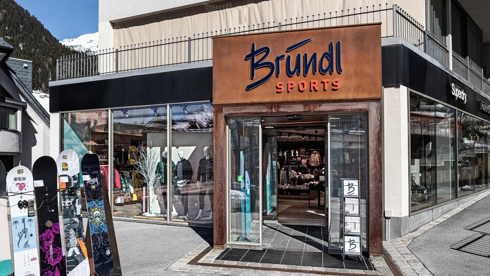A sports store named Bründl with display windows is visible. Outside, there are some snowboards.
