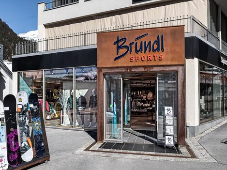 A sports store named Bründl with display windows is visible. Outside, there are some snowboards.