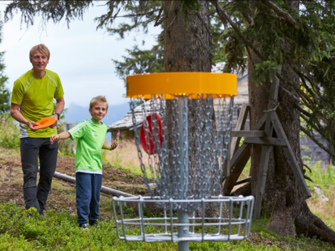 Ein Mann und ein Junge stehen in einem Wald und spielen Disc Golf. Im Hintergrund ist der Korb für das Spiel zu sehen.