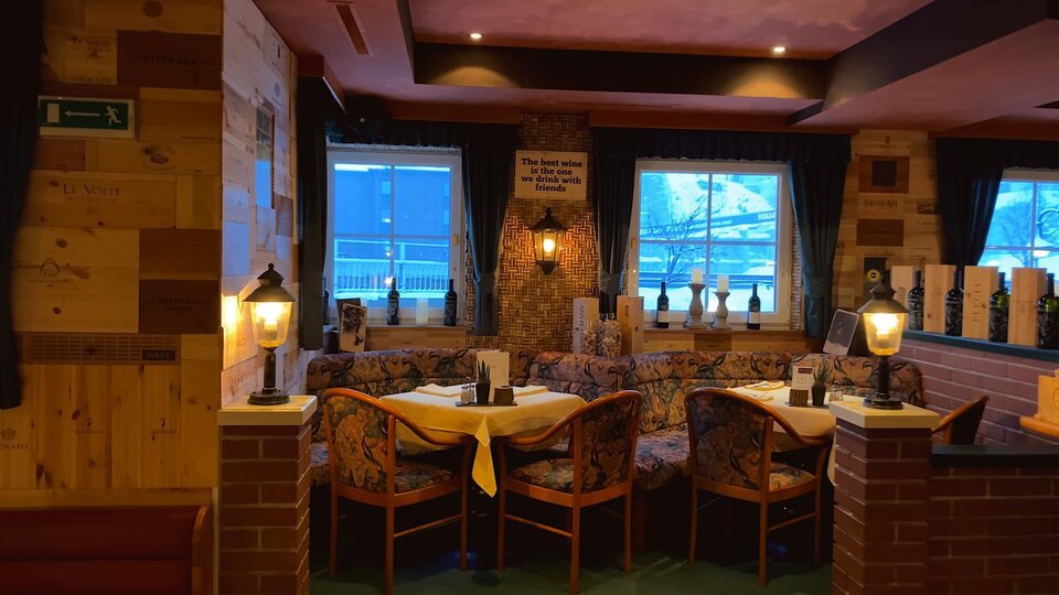 Ein gemütliches Restaurant mit Holzwänden und warmem Licht. Die Tische sind für Gäste vorbereitet und bieten eine einladende Atmosphäre.