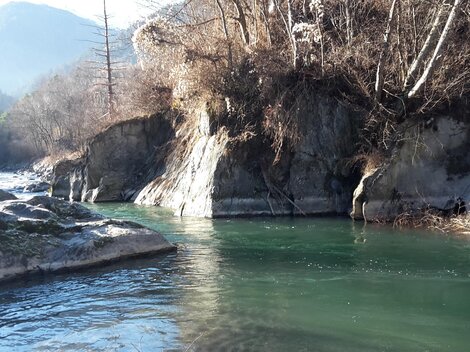 Ein ruhiger Fluss fließt zwischen felsigen Ufern. Im Hintergrund sind bewaldete Hügel zu sehen.