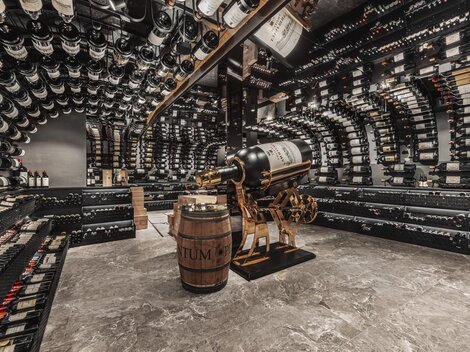 Ein eleganter Weinkeller mit vielen Regalen voller Weinflaschen. In der Mitte steht ein Fass und eine dekorative Weinpressmaschine.