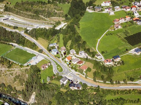 Eine Luftaufnahme einer ländlichen Gegend mit Wohnhäusern, Straßen und grünen Feldern. Die naturnahe Umgebung zeigt eine Mischung aus Wohngebieten und landwirtschaftlichen Flächen.