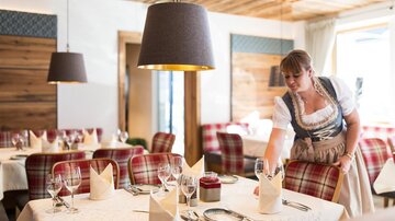 A cozy restaurant with an inviting atmosphere. A waitress sets the table with elegant glasses and napkins.