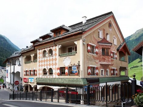 Ein charmantes Gebäude mit kunstvollen Wandmalereien in einer malerischen Berglandschaft. Die Straßen sind von Natur umgeben, und die Atmosphäre ist einladend.