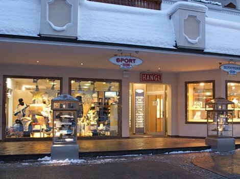 Ein Sportgeschäft mit beleuchteten Schaufenstern in einer schneebedeckten Straße. Der Eingangsbereich ist einladend und zeigt verschiedene Sportartikel.