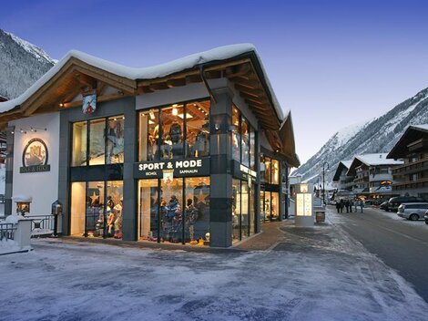 Ein modernes Geschäft in den Alpen, umgeben von schneebedeckten Bergen. Die Fassade ist großflächig verglast und einladend.