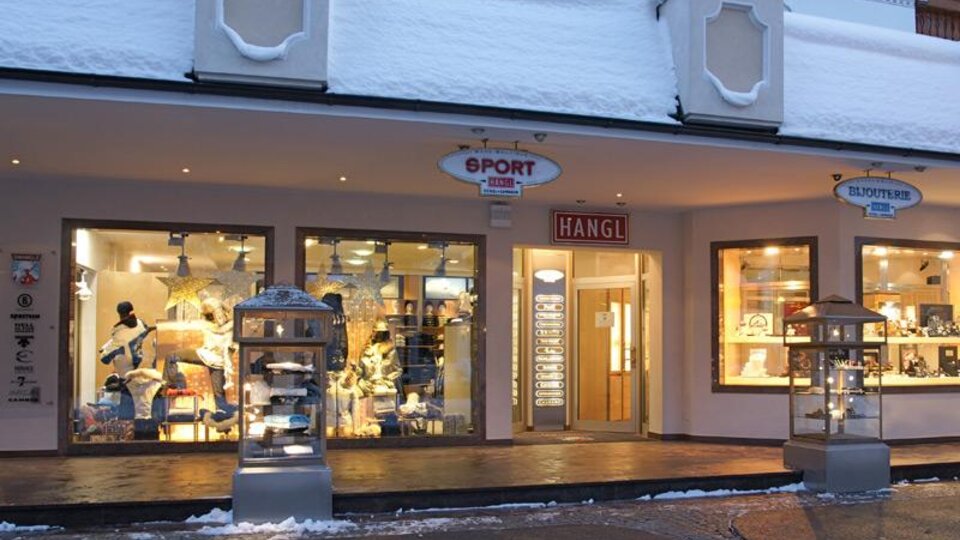Ein Sportgeschäft mit großen Fenstern, das in einer schneebedeckten Umgebung steht. Die Schaufenster zeigen Sportbekleidung und -ausrüstung.