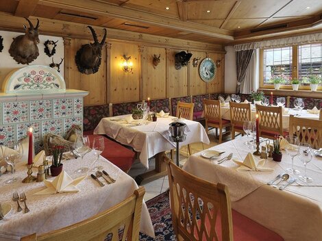 Ein gemütliches Restaurant mit Holzwänden und eleganten Tischdeckchen. Die Tische sind festlich gedeckt und die Dekoration umfasst traditionelle Jagdtrophäen.