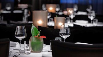 Ein elegantes Restaurant mit gedeckten Tischen und sanfter Beleuchtung. Auf dem Tisch steht eine dekorative Pflanze mit einem Cocktailglas.