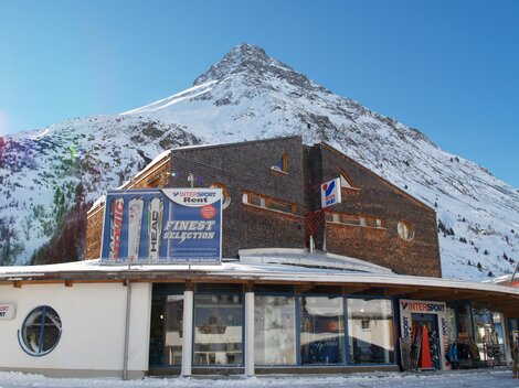 Ein modernes Gebäude vor einem schneebedeckten Berg. Der klare Himmel und die Winterlandschaft schaffen eine malerische Aussicht.