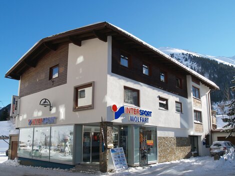 Ein sportliches Geschäft in einem schneebedeckten Gebiet. Die Fassade zeigt große Fenster und eine klare Beschilderung.