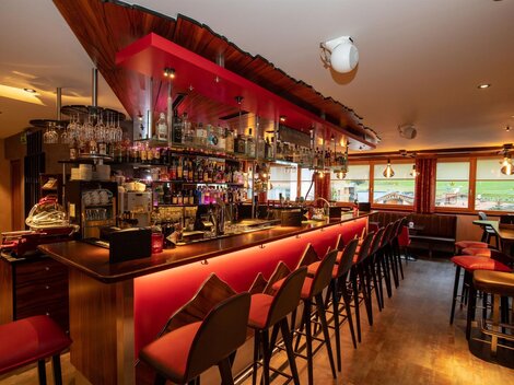 Eine moderne Bar mit einer einladenden Einsatz von rotem Licht. Die Theke ist gut bestückt und es gibt viele Stühle, die auf Gäste warten.
