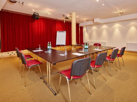 Ein modern ausgestatteter Besprechungsraum mit einem großen Tisch und roten Stühlen. Die Wände sind mit rotem Vorhang und einer sanften Beleuchtung dekoriert.