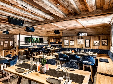 Ein modernes Restaurant mit Holzinterieur und gemütlicher Atmosphäre. Die Tische sind elegant gedeckt und bieten Platz für viele Gäste.
