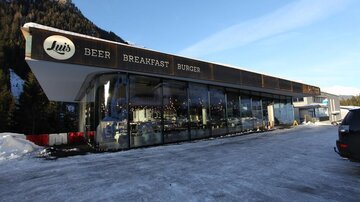 Ein modernes Restaurant mit großen Fenstern in einer winterlichen Umgebung. Das Schild zeigt die Angebote „Beer“, „Breakfast“ und „Burger“.