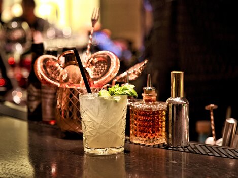 A delicious cocktail with fresh mint is on an elegant bar. In the background, various bottles and utensils are visible.
