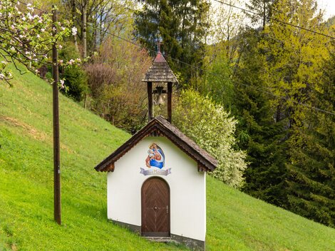 Eine kleine Kapelle steht auf einer grünen Wiese. Umgeben von Bäumen vermittelt sie eine ruhige und idyllische Atmosphäre.