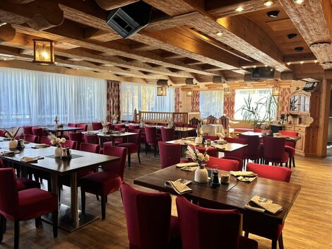 Ein gemütliches Restaurant mit Holzelementen und roten Stühlen. Die Tische sind freundlich gedeckt und die Fenster bieten einen Blick nach draußen.