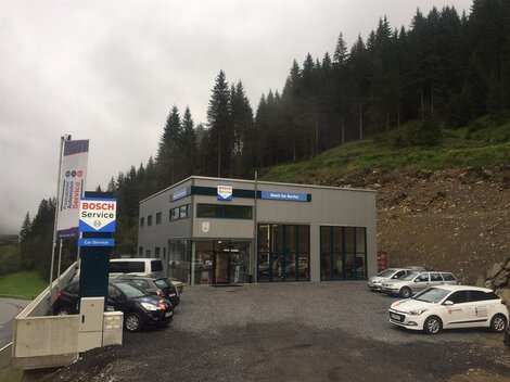 Ein modernes Servicegebäude von Bosch, umgeben von Wälder und Bergen. Auf dem Parkplatz stehen mehrere Autos.