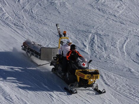 Ein Schneemobil fährt über den Schnee. Auf dem Schneemobil sind zwei Personen, die Ausrüstung für medizinische Notfälle transportieren.