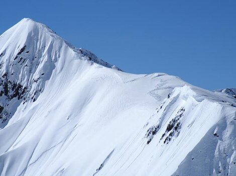 Ein schneebedeckter Berg unter einem klaren blauen Himmel. Die Landschaft ist majestätisch und beeindruckend.