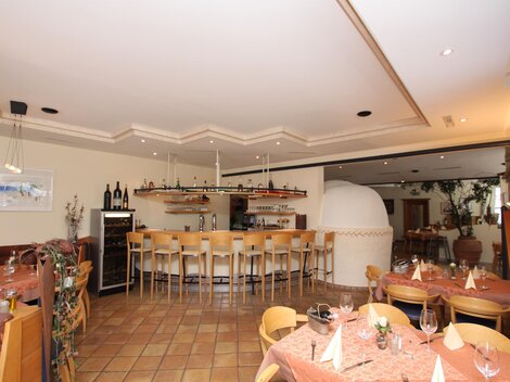 Ein gemütliches Restaurant mit einer Bar und Holzmöbeln. Die Tische sind elegant gedeckt und es befindet sich ein schöner Innenbereich.