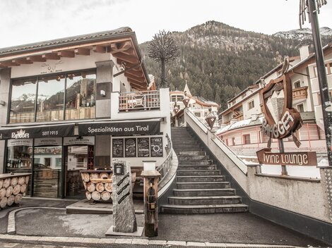 Ein gemütlicher Ort mit Holzmöbeln und einem einladenden Restaurant. Im Hintergrund sind die Berge sichtbar, was eine alpine Atmosphäre schafft.