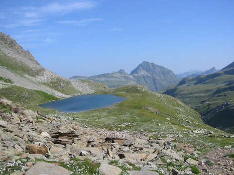 Eine malerische Berglandschaft mit einem klaren, blauen See. Im Hintergrund erheben sich majestätische Berge unter einem blauen Himmel.