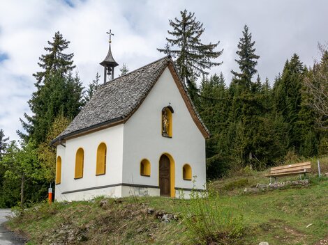 Eine kleine, weiße Kapelle steht inmitten von Bäumen. Der Himmel ist bewölkt und die Umgebung ist grün. | © Bernhard Gruber – Photography